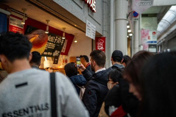 Crowd of people waiting in line outside a food vendor in a bustling urban area.