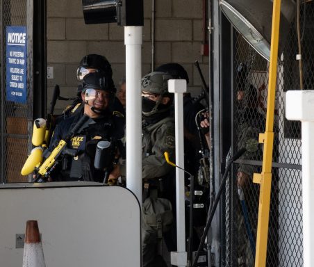 Group of law enforcement officers in tactical gear preparing at a security checkpoint.