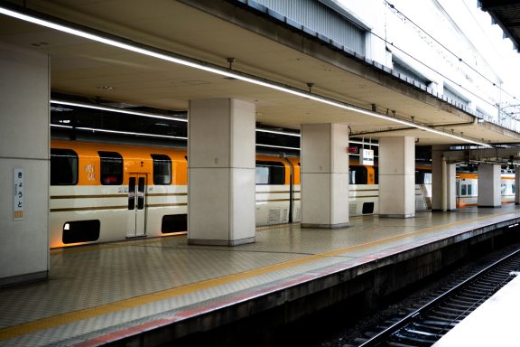 Train at a platform with yellow exterior and concrete pillars.
