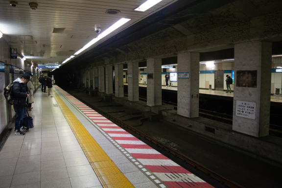Empty subway station platform with tracks and a few waiting passengers.