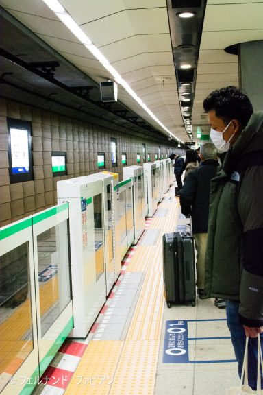 People waiting at a subway platform with a train arriving, some wearing masks.